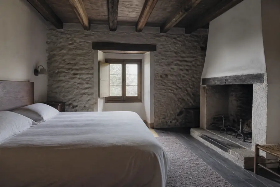 Dormitorio con muro de piedra, vigas de madera y chimenea de piedra
